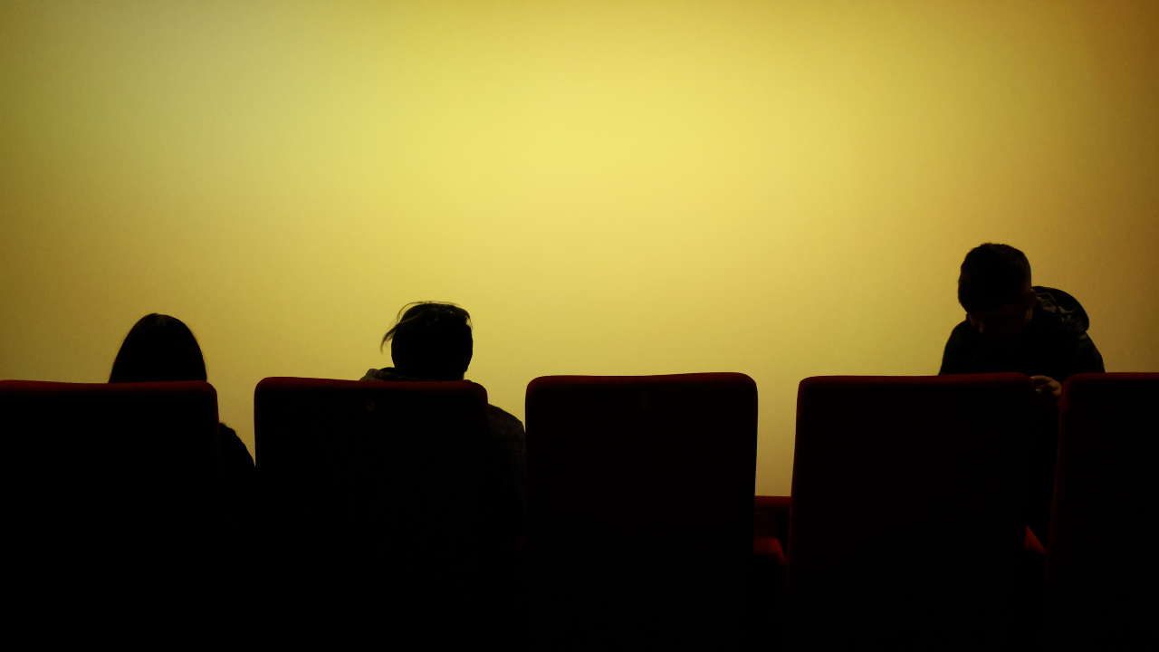 Des personnes sont assises dans une salle de cinéma face à un écran jaune