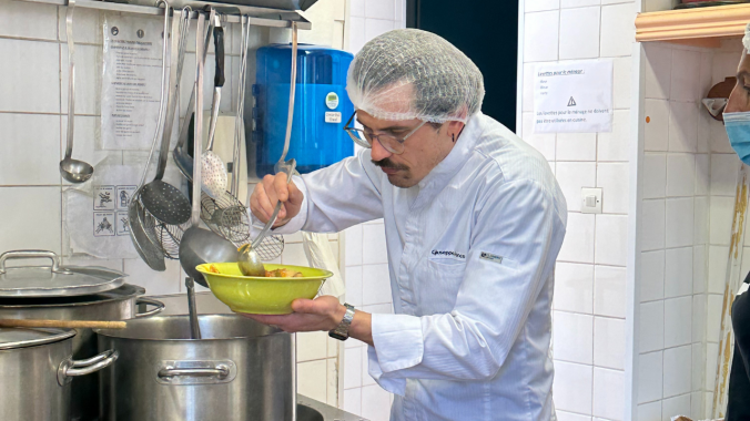 Un chef cuisinier avec une charlotte sur la tête goûte un plat.